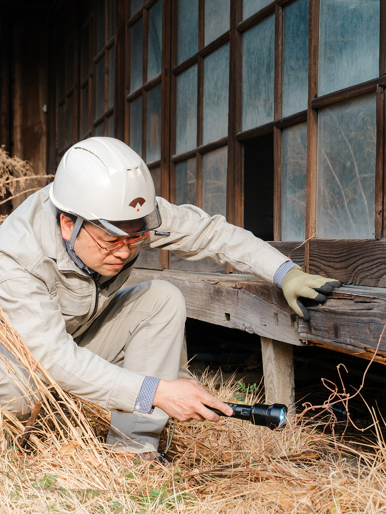 作業着姿の専門家が古民家の柱を調査している様子