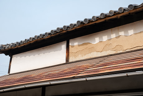 外壁の漆喰が剥がれ土壁が露出している古民家の外観